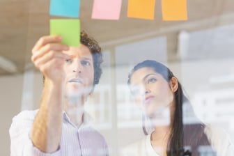Businessman and businesswoman sticking adhesive notes on glass wall in office.jpeg